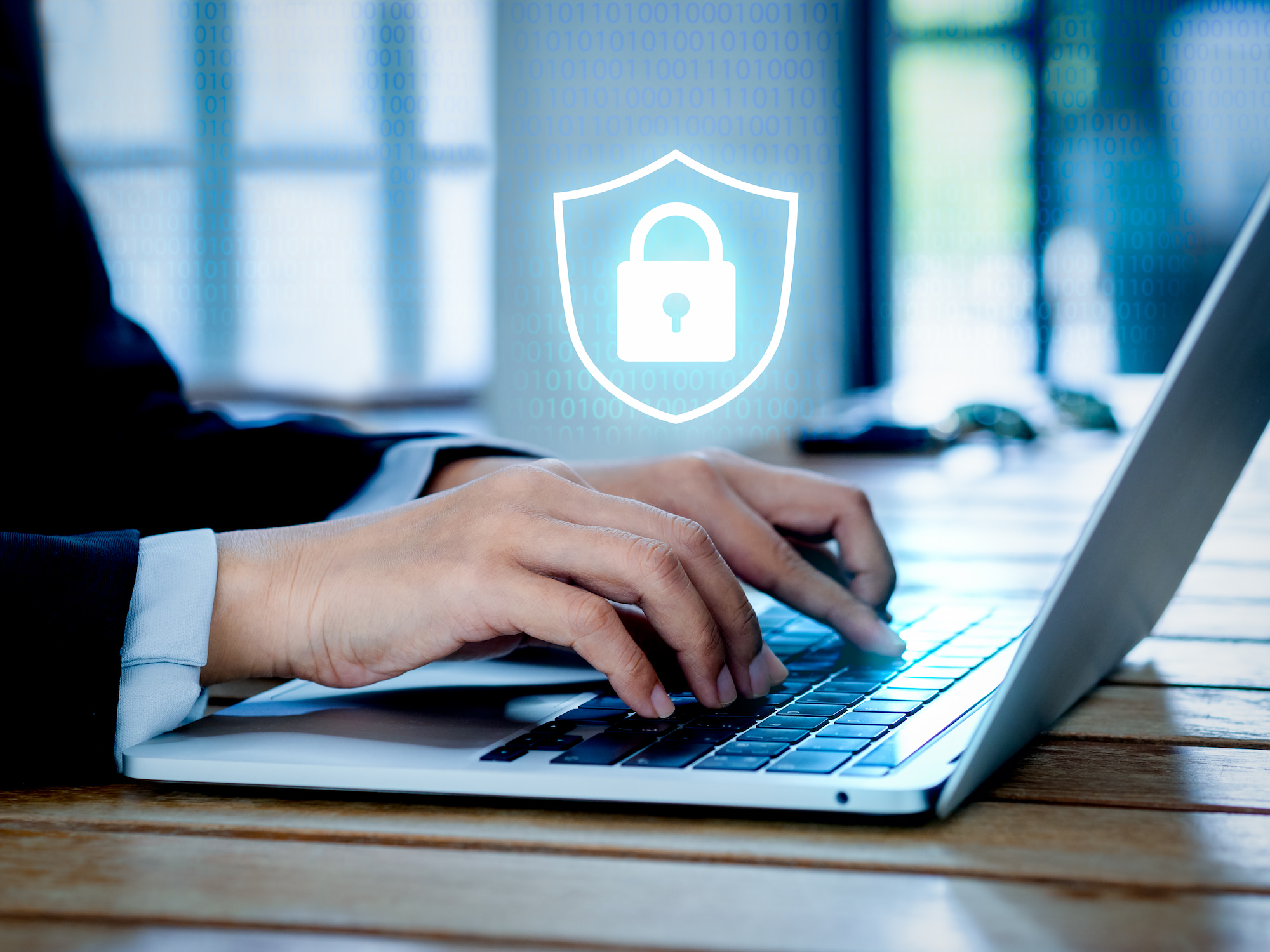 Seguridad informática: Hombre escribiendo en un portátil con un símbolo flotante de un candado dentro de un escudo representado la ciberseguridad