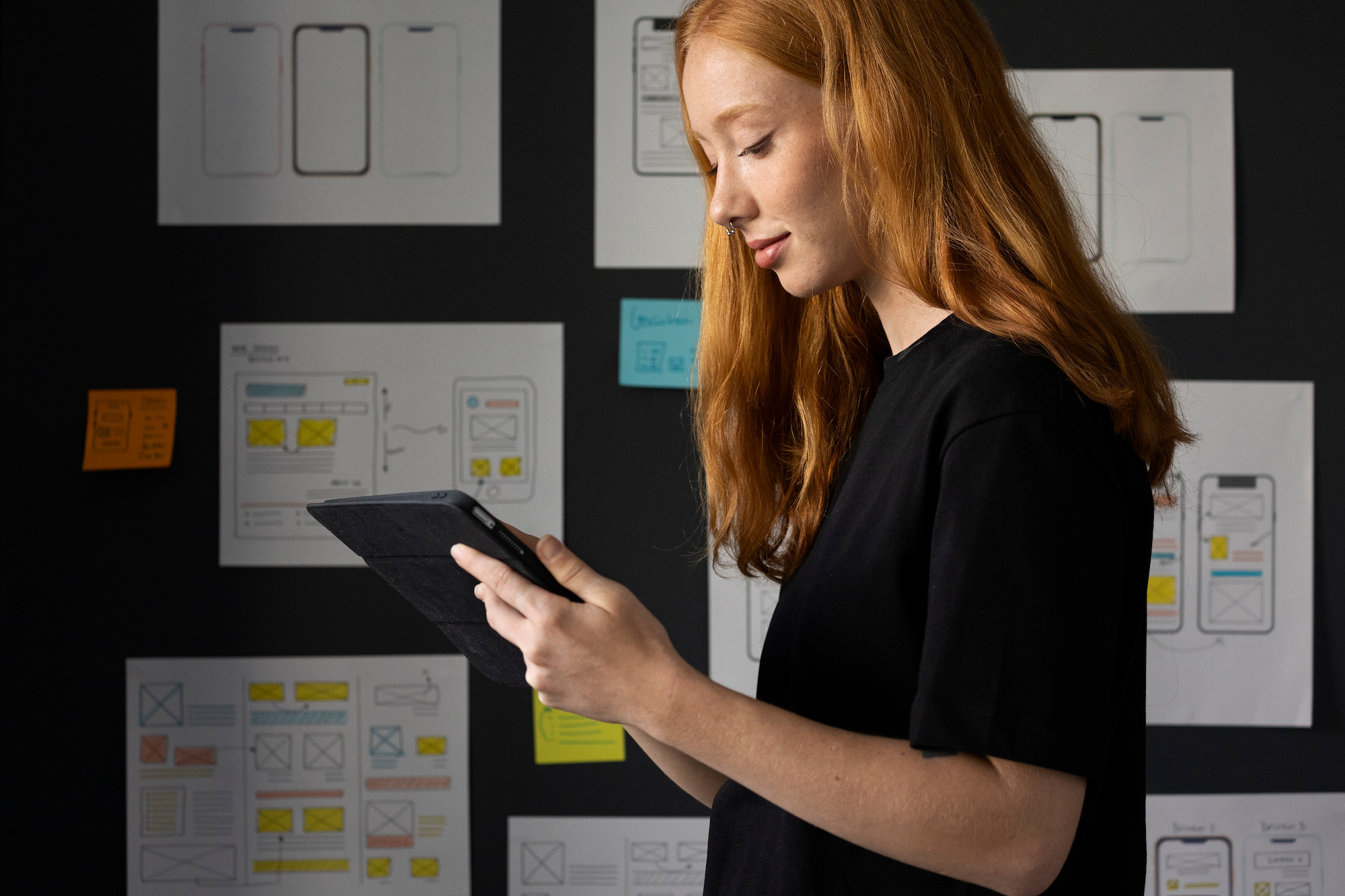 Chica sosteniendo una tablet frente a un muro de planificación, sugiriendo una sesión de lluvia de ideas para el desarrollo de apps.