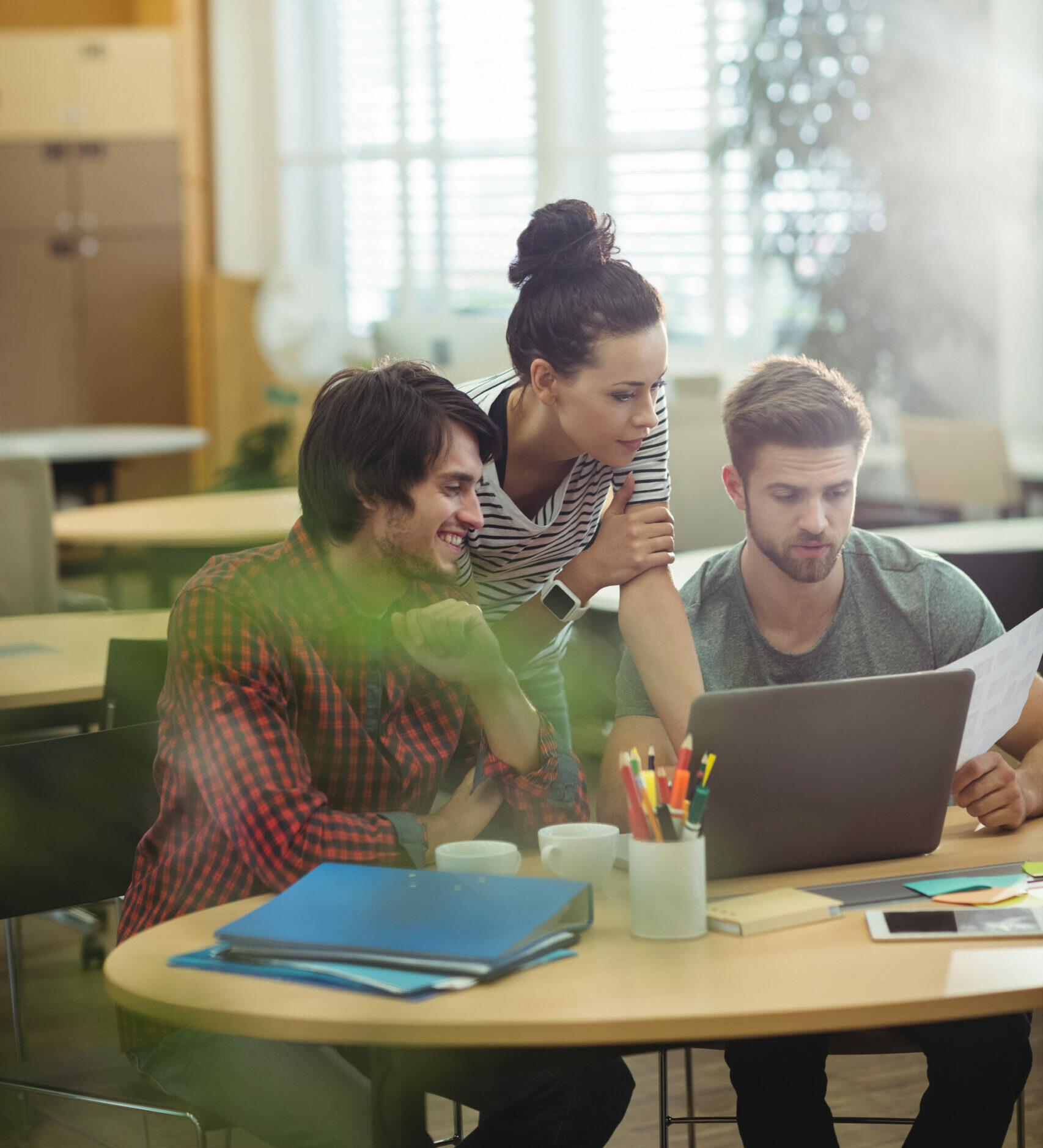 Tres personas colaborando alrededor de una mesa con un ordenador portátil, indicando el trabajo en equipo en el ‘desarrollo web’.