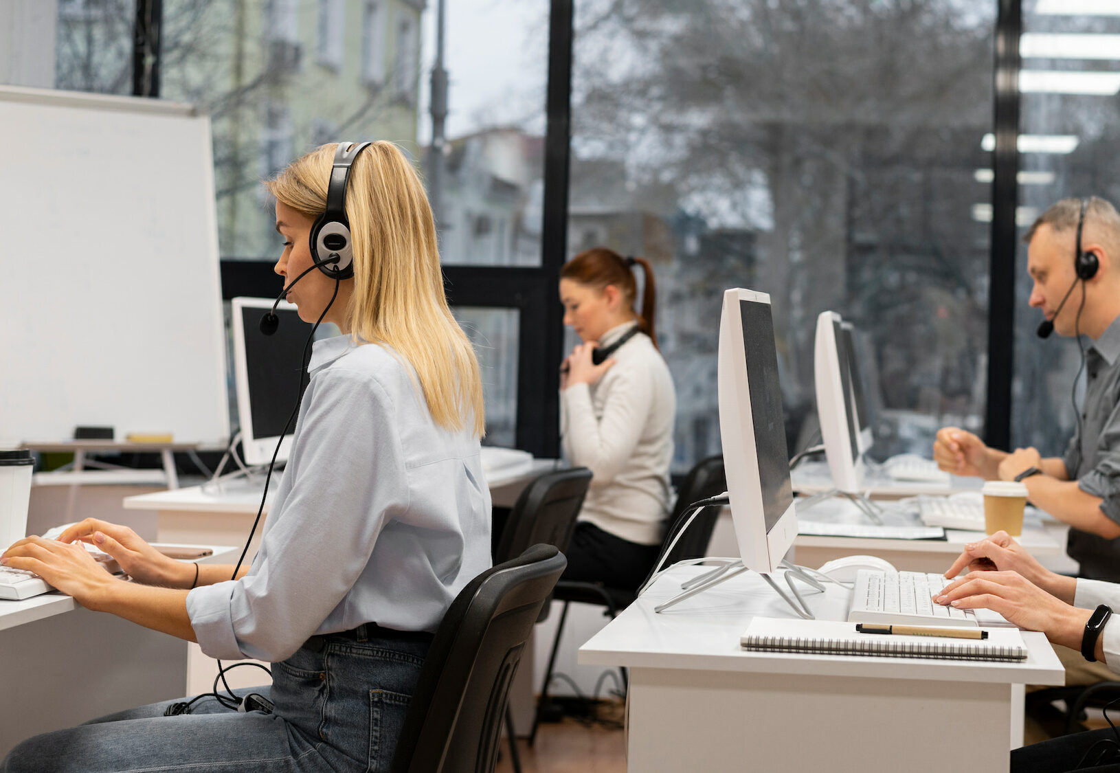 Cuatro profesionales trabajando en sus escritorios con ordenadores de sobremesa en un entorno de oficina.