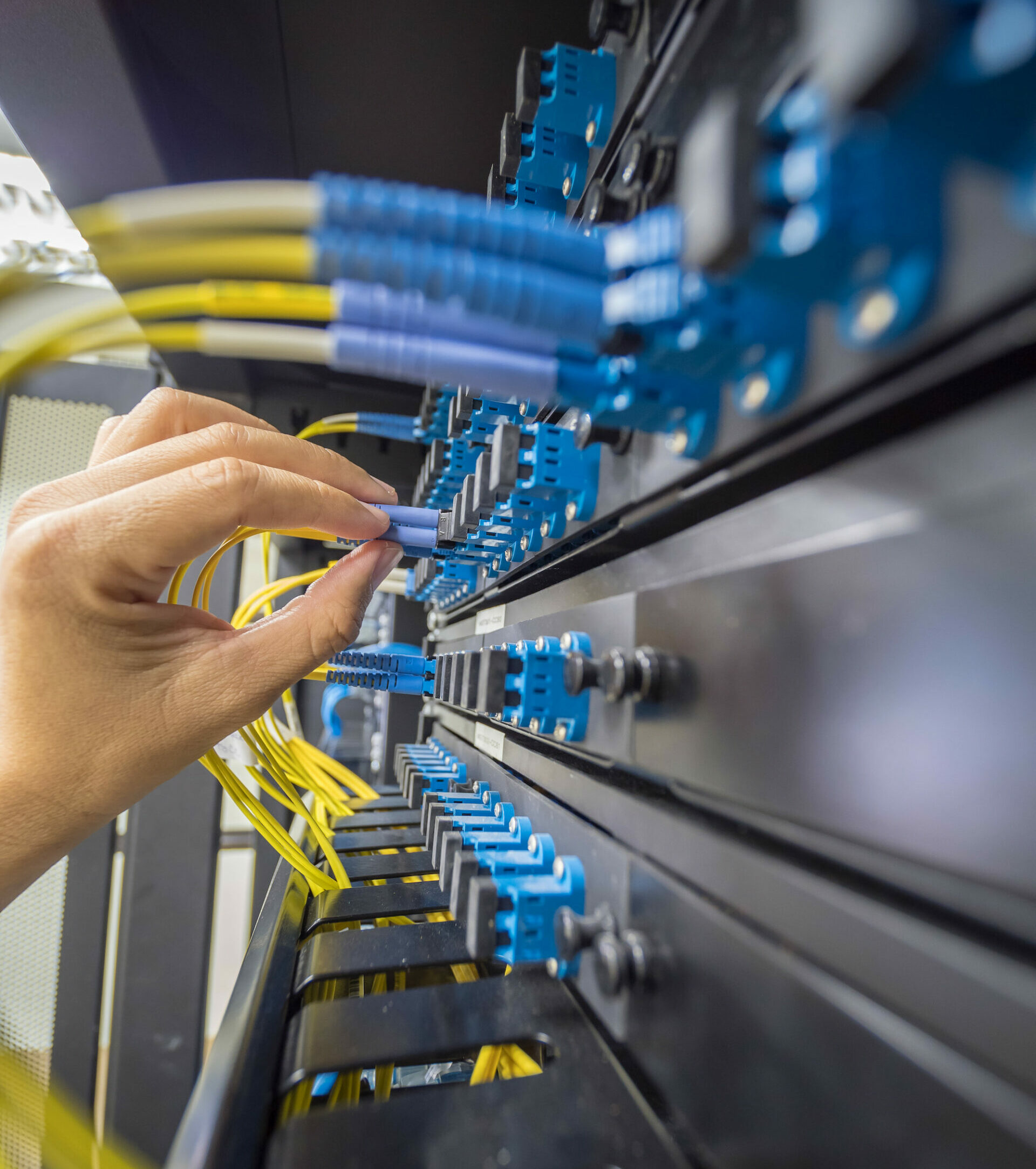 Primer plano de una instalación de fibra con una mano conectando un cable de red en un panel de parcheo.