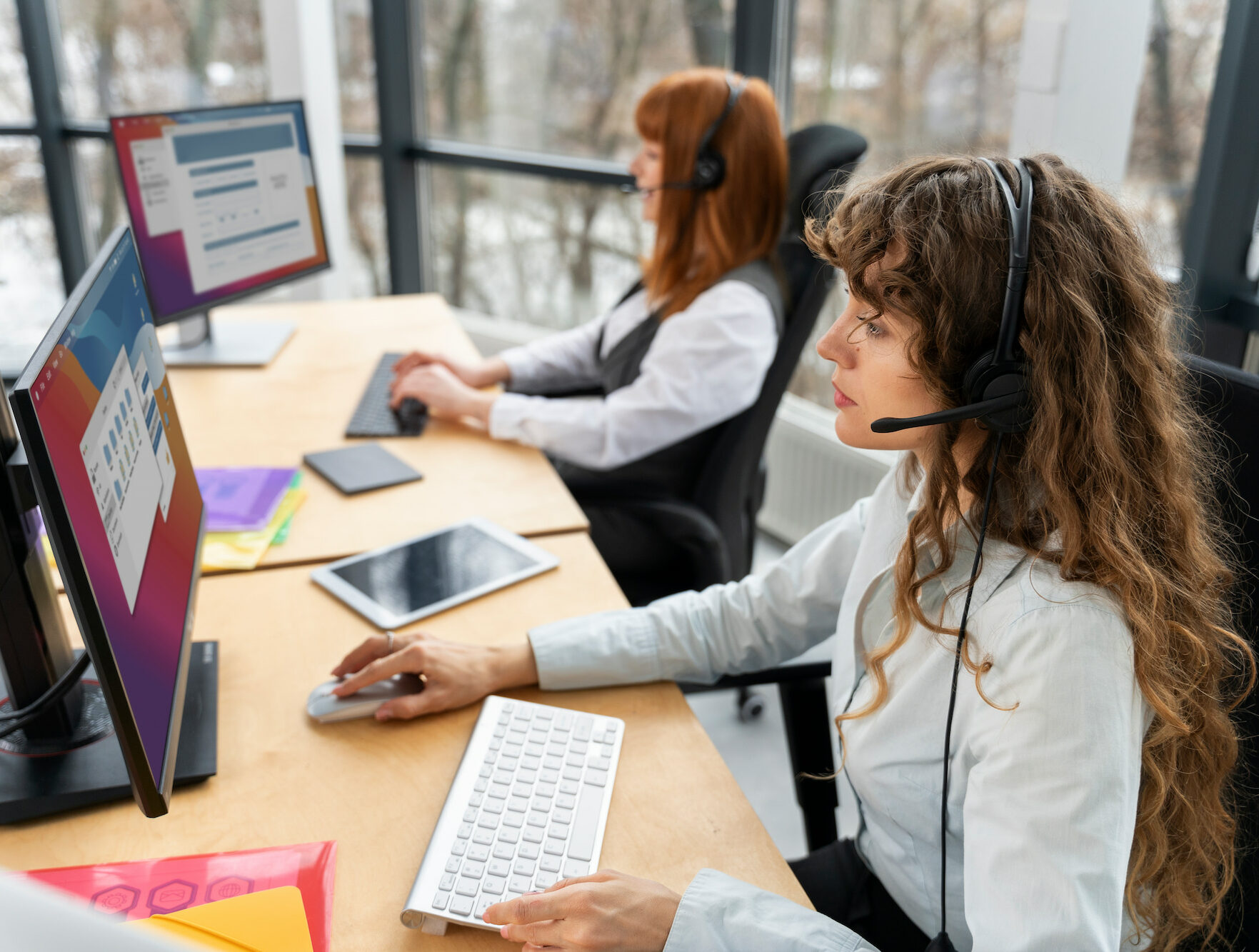 Dos chicas trabajando en un entorno de oficina con computadoras, representando el servicio de centralita virtual.