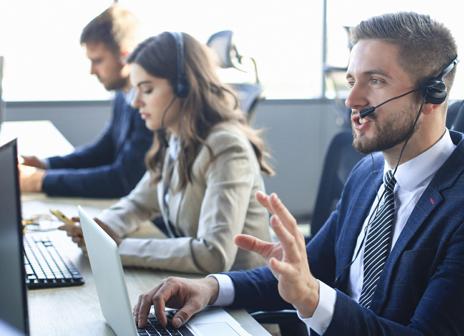 Grupo de individuos en un centro de llamadas, sentados en escritorios con computadoras y usando auriculares, representando el uso de troncales sip.