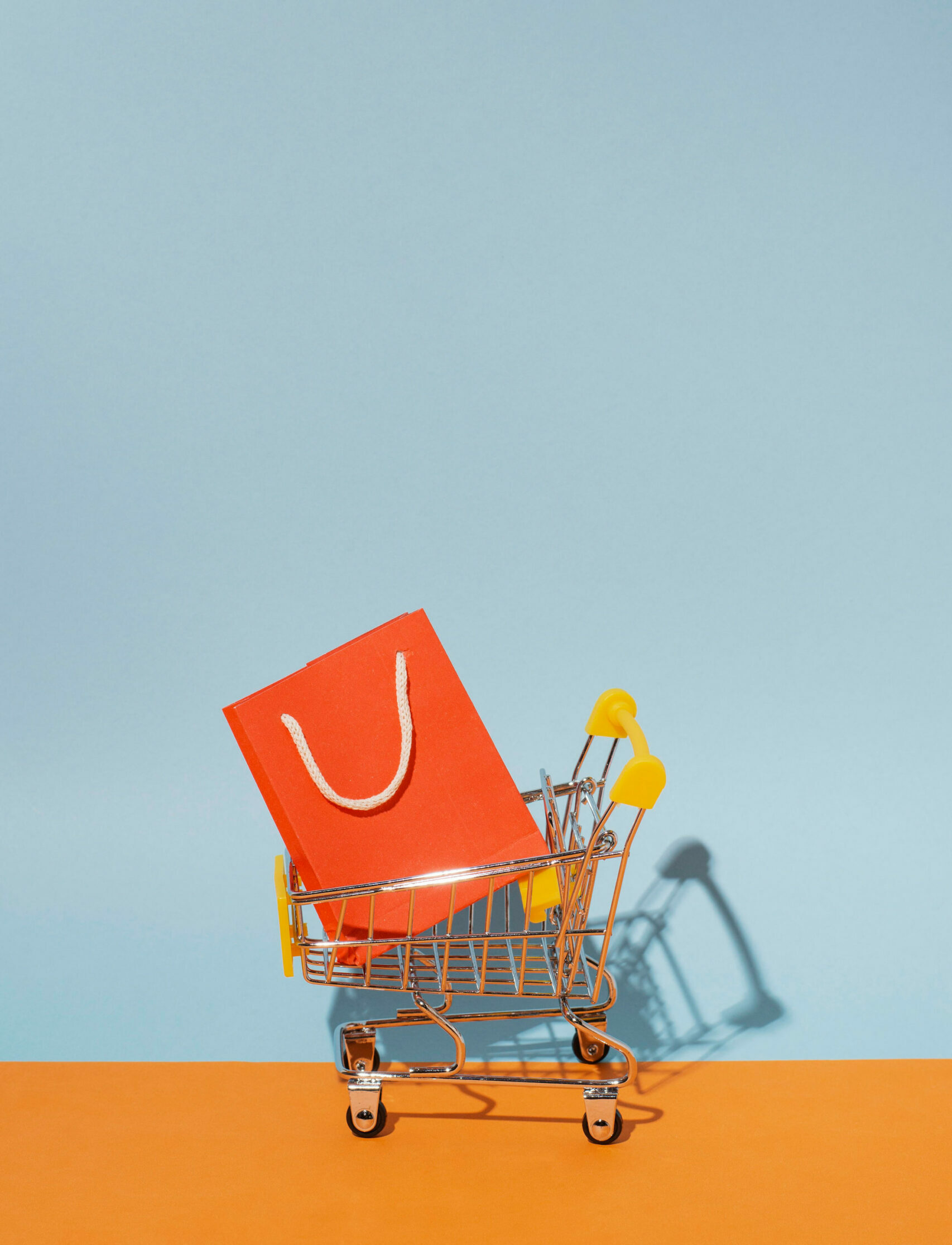 Carrito de compras miniatura con una sola bolsa de compras naranja en un fondo azul.