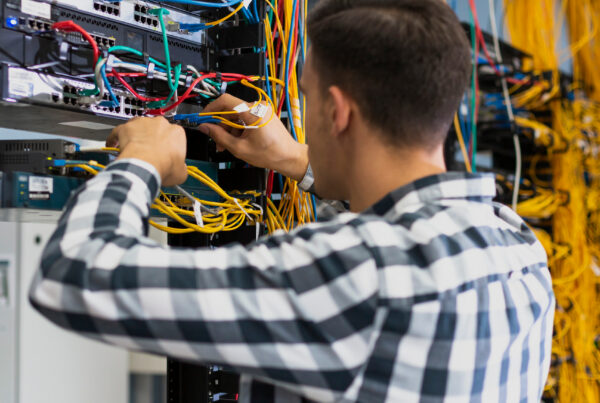 Profesional de TI trabajando en un rack de servidores con numerosos cables de una instalación de fibra.