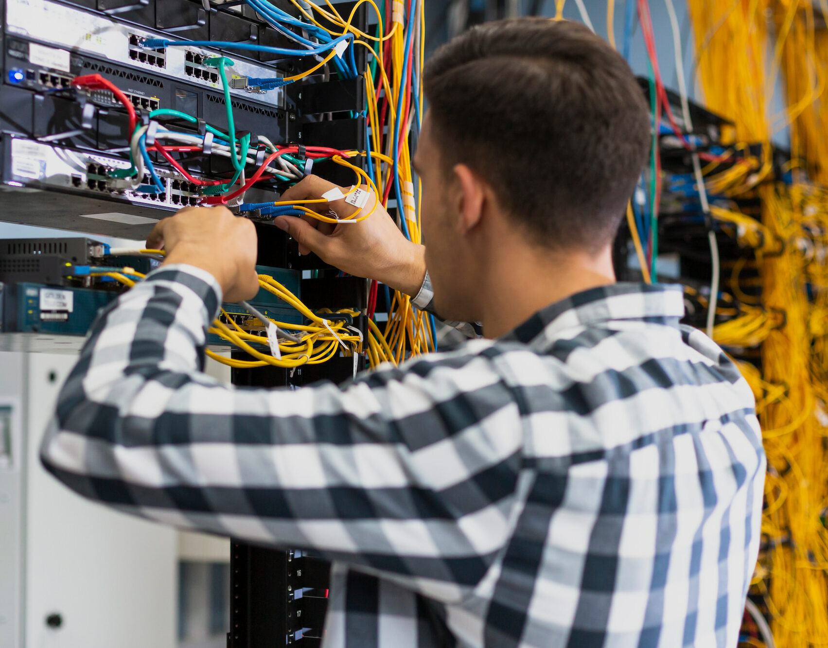 Profesional de TI trabajando en un rack de servidores con numerosos cables de una instalación de fibra.